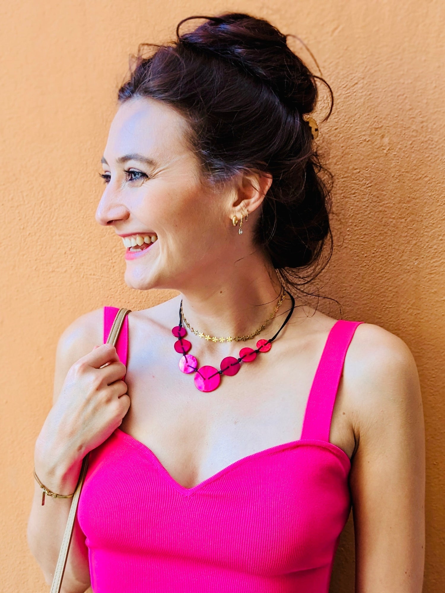 Woman wearing a bright pink top and colorful skirt against a beige wall